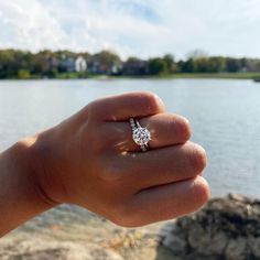 a person's hand holding a diamond ring near the water