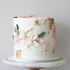 a white cake with pink and gold flowers on it sitting on top of a wooden stand