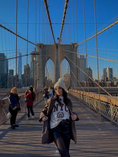 a woman walking across a bridge in front of the brooklyn bridge with other people on either side