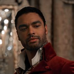 a close up of a person wearing a red jacket and white shirt with lights in the background