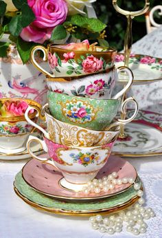 a stack of tea cups and saucers with flowers in the background on a table