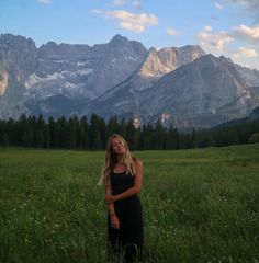 a woman standing in a field with mountains in the background