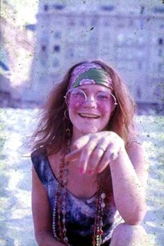 a woman sitting on the ground in front of a building wearing glasses and beaded headband