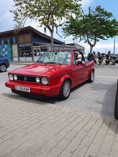 a red car is parked on the side of the road in front of other cars