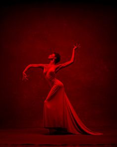 a woman in a long red dress is dancing with her arms outstretched and legs spread out