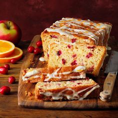 sliced loaf of orange cranberry bread with icing on cutting board next to fruit