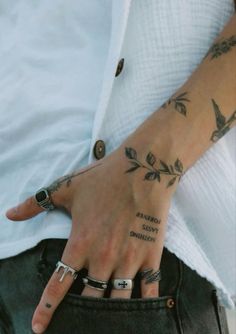 a person with tattoos on their hands and fingers is holding onto his jeans pocket while wearing a white shirt