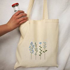 a person holding a tote bag with blue flowers on it and a spray bottle in their hand