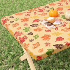 an orange table cloth with fall leaves on it and two pumpkins sitting on top