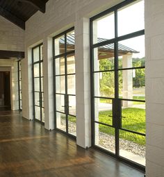 an empty room with wooden floors and large windows on both sides, looking out onto a grassy area