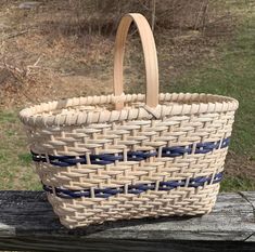 a woven basket sitting on top of a wooden bench next to a field and trees