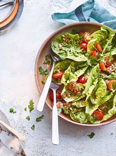 a bowl filled with lettuce and tomatoes next to spoons on a table