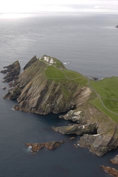 an island in the middle of water with green grass and rocks on it's sides