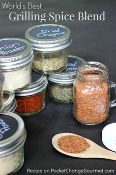 several jars filled with spices sitting on top of a black table next to a wooden spoon