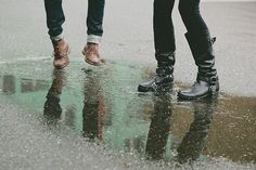 two people are standing in the rain with their feet up and one is holding an umbrella