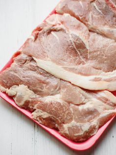 two pieces of raw meat sitting on top of a pink plastic tray next to each other