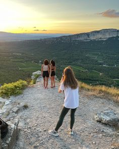 three girls standing at the top of a mountain looking out into the valley and mountains