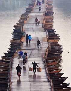 several people walking on a dock with canoes attached to it and one person riding a bike