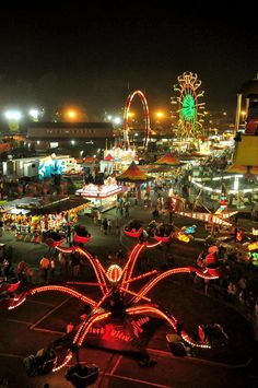 an aerial view of a fair at night with lights on and rides in the background