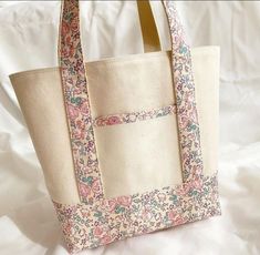 a white bag with pink and blue flowers on the inside is sitting on a bed