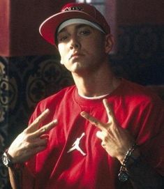 a young man in a red shirt and hat making the peace sign with his hands