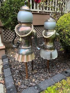 two metal vases sitting on top of each other in front of a garden area