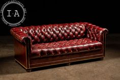 a red leather couch sitting on top of a brown floor next to a black wall