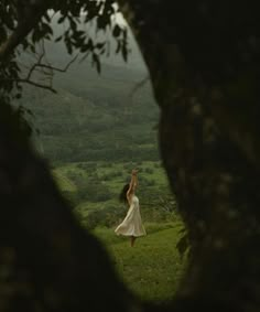 a woman in a white dress standing on top of a lush green field next to a forest