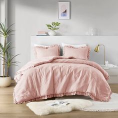 a bed with pink comforter and pillows in a room next to a potted plant