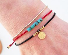 three different bracelets on someone's arm, one with a gold disc and the other red string