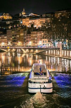 a white boat traveling down a river next to a city at night with buildings in the background