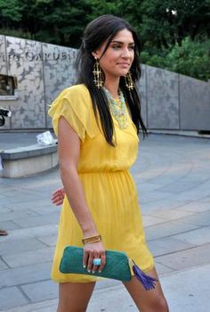 a woman in a yellow dress is holding a green purse and walking down the street