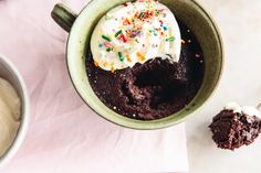 a cup filled with ice cream next to a spoon and bowl full of chocolate cake