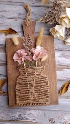 some flowers are in a vase on a wooden board with dried grass and feathers around it