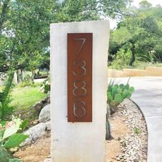 a sign that is on the side of a road in front of some plants and trees