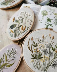 four embroidery hoops with flowers on them sitting on top of a wooden table next to an open book