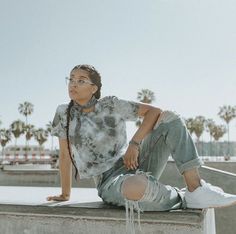 a woman sitting on top of a cement wall next to palm trees and wearing glasses