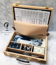 an open wooden box with various items inside on a marble counter top next to a pair of scissors