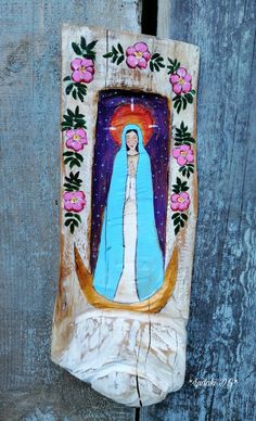 an image of the virgin mary with flowers on it's side, hanging from a wooden fence