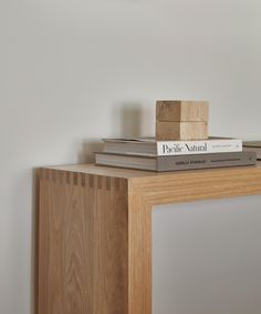 stack of books sitting on top of a wooden table next to a white wall and light fixture