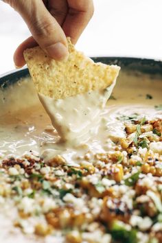 a person dipping tortilla chips into a bowl of soup with cheese and other toppings