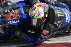 a man riding on the back of a blue motorcycle down a race track next to another person