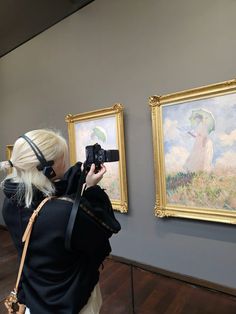 a woman taking a photo of paintings on the wall with a camera in front of her