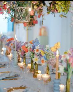 a long table with flowers and candles in vases on top of it, along with other place settings