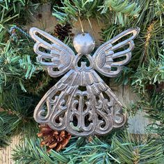 an angel ornament hanging from a christmas tree with pine cones in the background