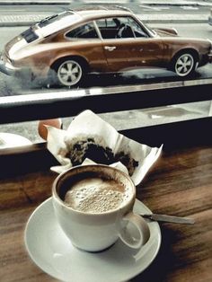 a cup of coffee sitting on top of a saucer next to a window with a car in the background