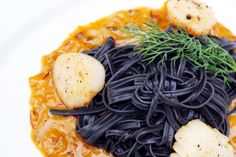 a white plate topped with pasta and scallops on top of it's black sauce