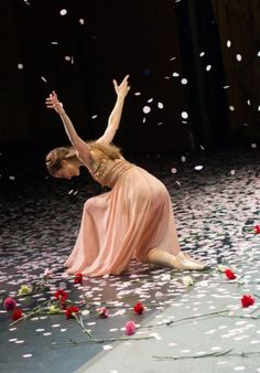 a woman sitting on the ground surrounded by flowers and petals with her arms in the air