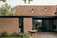 a brick building with two windows and a wooden table in front of the door is surrounded by greenery