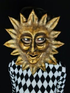 a person wearing a gold mask and checkered shirt with black hair in front of a black background